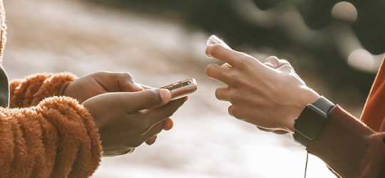 close up of two young adults hands typing on smart phones in front of each other